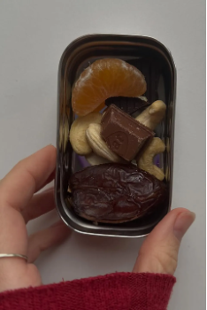 A snack tin the size of a sardine can with one segment of a satsuma, a few cashews and raisins and one square of chocolate